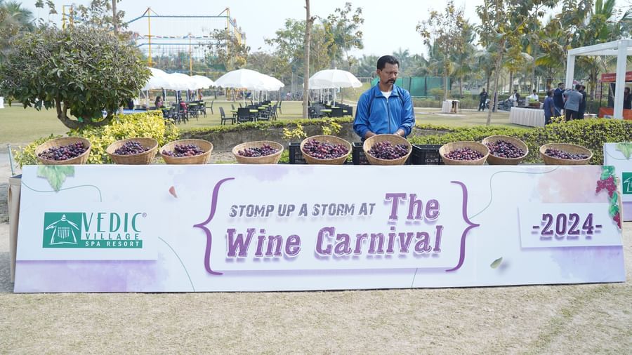 A banner for 'The Wine Carnival' with '2024' displayed is set up outdoors, with people gathered around it | Vedic Village Spa Resort, Kolkata