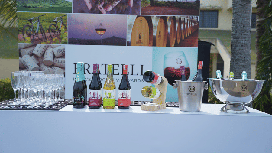 A Fratelli wine brand display setup at Vedic Village Spa Resort featuring wine bottles glasses and a branded backdrop with vineyard imagery in an indoor event setting.
