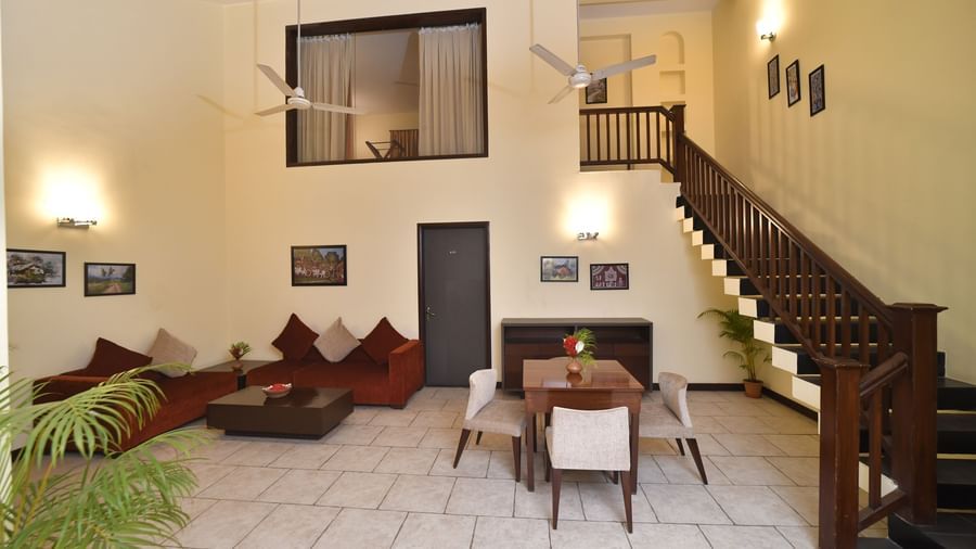 A living room with high ceilings includes a staircase, comfortable sofas, and a dining table set for a meal Green Villas