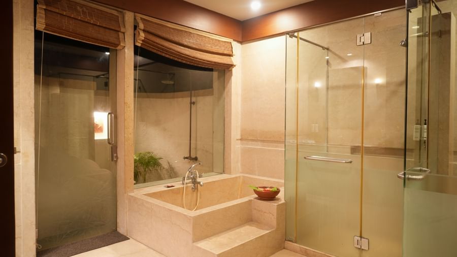 Glass-panelled shower room in the Lake View Villa at Vedic Village Spa Resort with a bathtub, shower cubicle, and a glass door opening to an outdoor shower area.