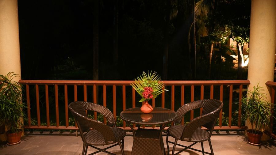 Night-time view of the balcony in the One-Bedroom Suite at Vedic Village Spa Resort, with lounge chairs and wooden railing.