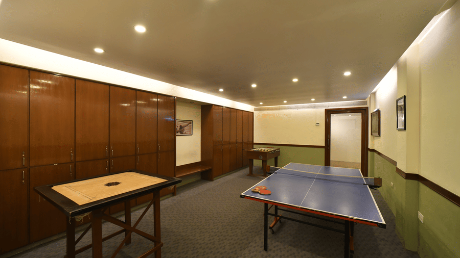 An indoor recreation room at Vedic Village Spa Resort featuring a table tennis table wooden wall panels recessed ceiling lights and a long corridor in a well-lit setting.