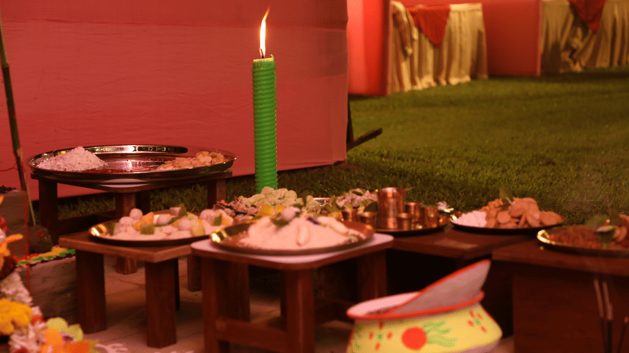 A traditional food display setup at Vedic Village Spa Resort featuring multiple dishes arranged on low wooden tables with a candle and green backdrop in a warmly lit setting.