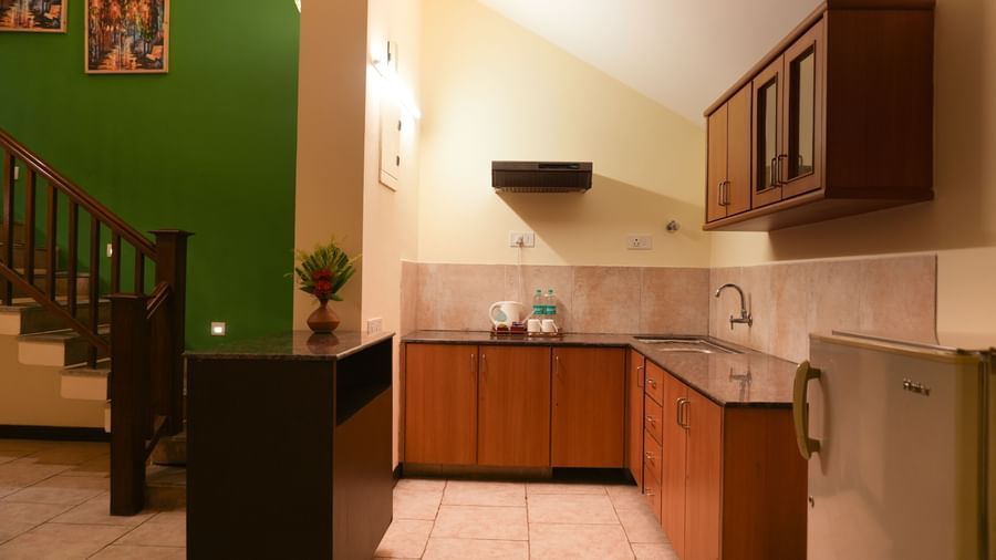 Compact kitchen in the Retreat Villa at Vedic Village Spa Resort with a mini fridge, wooden cabinets, sink area, and an electric kettle.