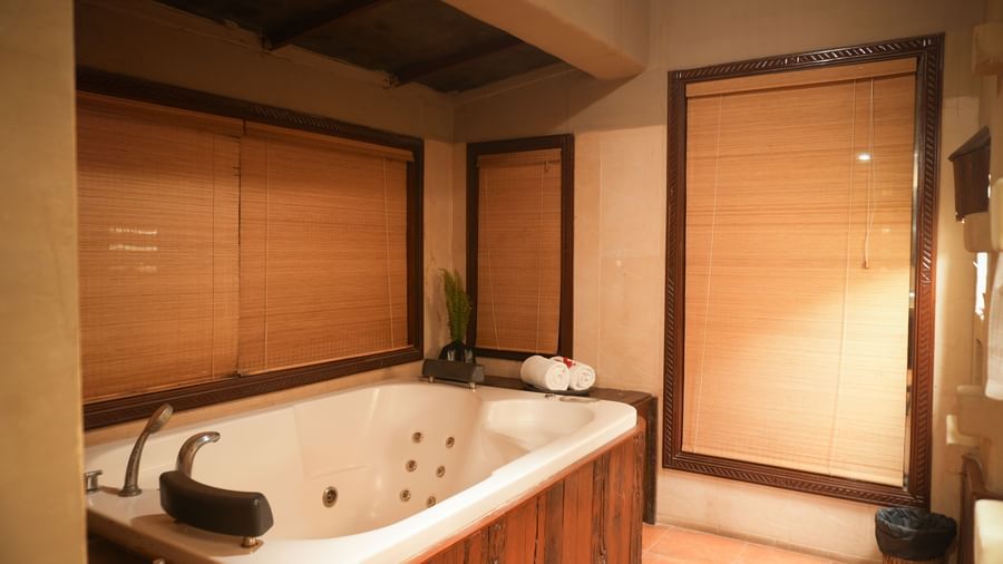 Wooden panelled jacuzzi in the Zamindar Suite at Vedic Village Spa Resort, set against brown flooring and brown roll-down blinds.