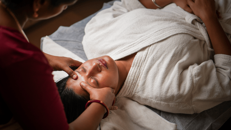 Therapist performing a gentle ayurvedic head massage on a female guest lying on a treatment table at Vedic Village Spa Resort Kolkata.