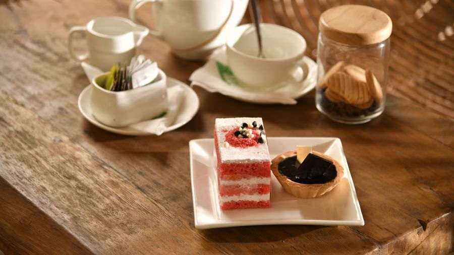 A tea set with cups, saucers, and a teapot is arranged on a table alongside a dessert | Chai