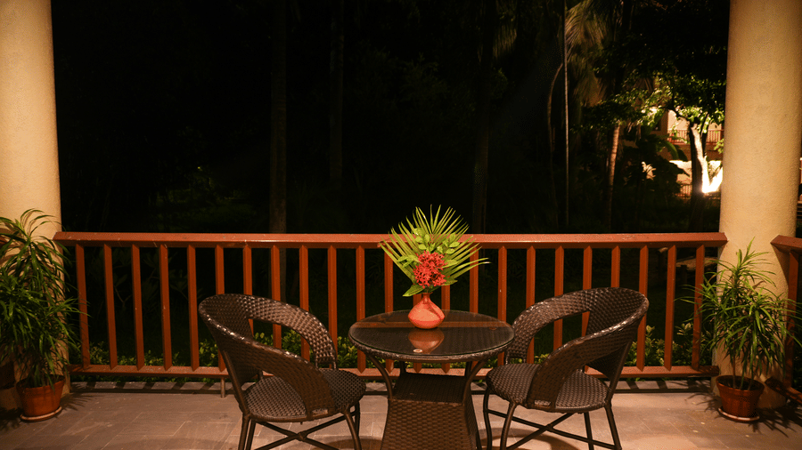 Night-time view of the balcony in the One-Bedroom Suite at Vedic Village Spa Resort, with lounge chairs and wooden railing.