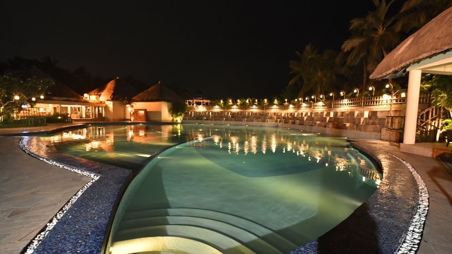 A swimming pool area is illuminated at night, surrounded by resort-style architecture