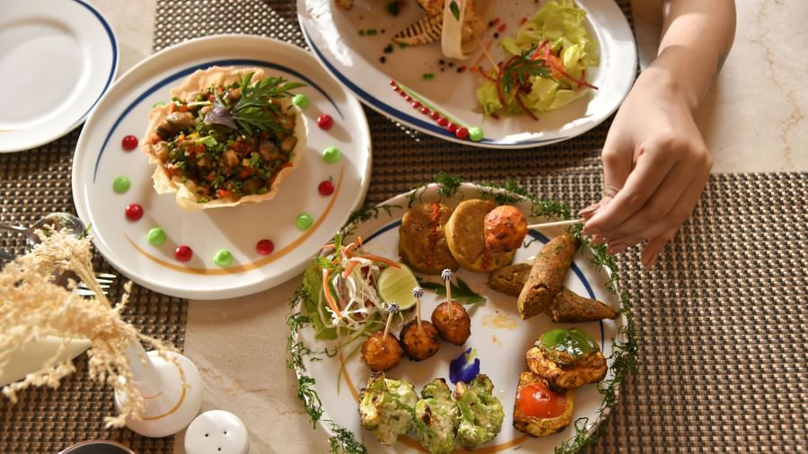 Hands are seen reaching for food served on plates, indicating a meal | Yagna
