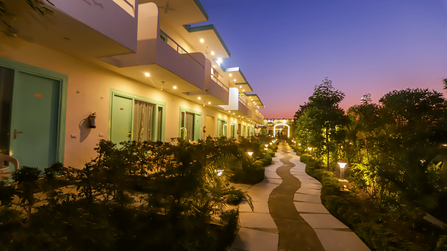An evening view along a path at Vedikant Resorts The Mallard Corbett shows rooms with lit balconies.