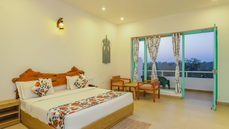 A cosy bedroom at Vedikant Resorts The Mallard Corbett includes a bed, chairs, and a view through the balcony.