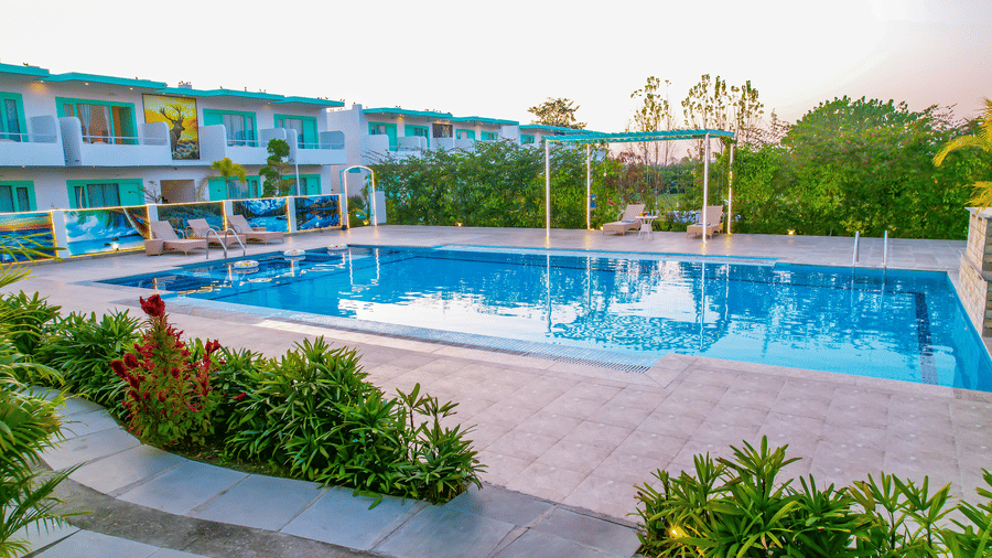 View of a swimming pool with buildings, trees and clear blue sky in the background - Vedikant Resorts The Mallard Corbett.