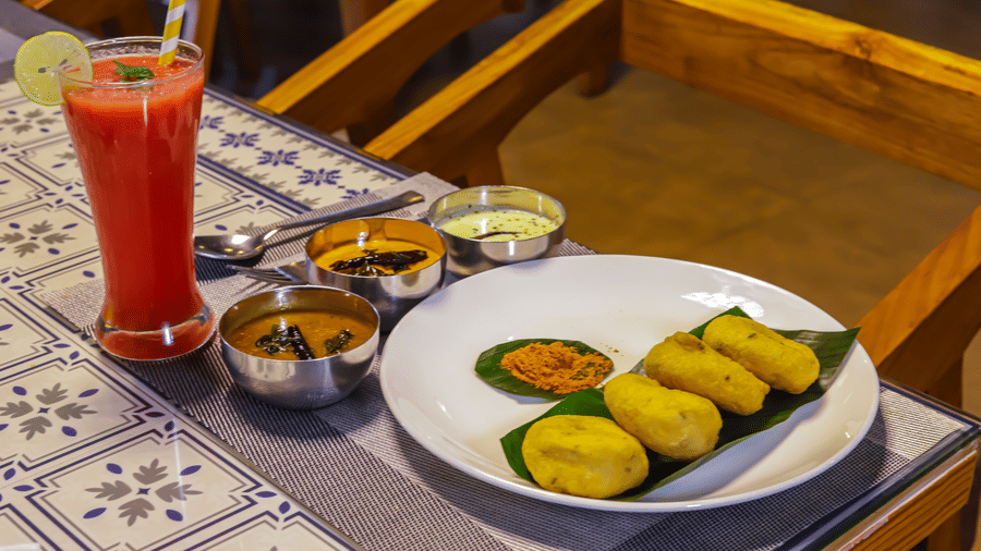 A plate of food with side dishes and a drink are arranged on a table with a patterned cloth at Vedikant Resorts The Mallard Corbett.