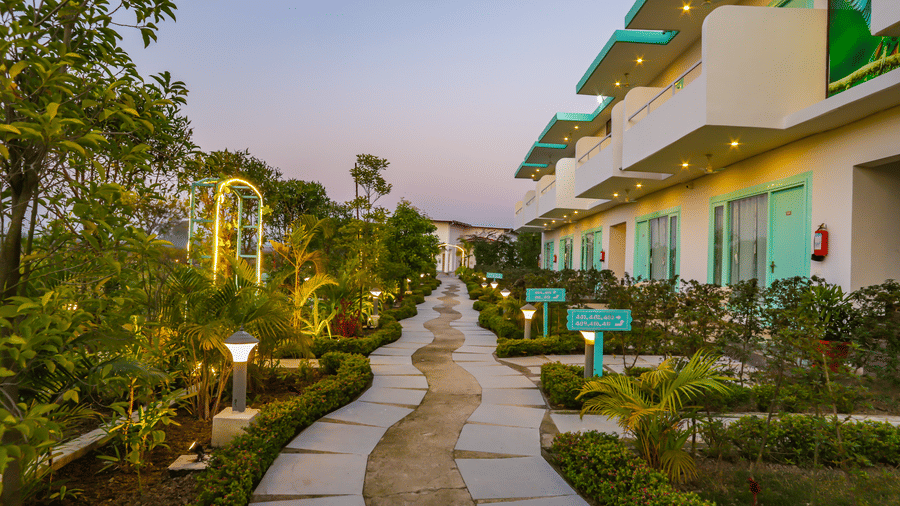 A pathway illuminated at dusk winds through the grounds of Vedikant Resorts The Mallard Corbett, showcasing the buildings.