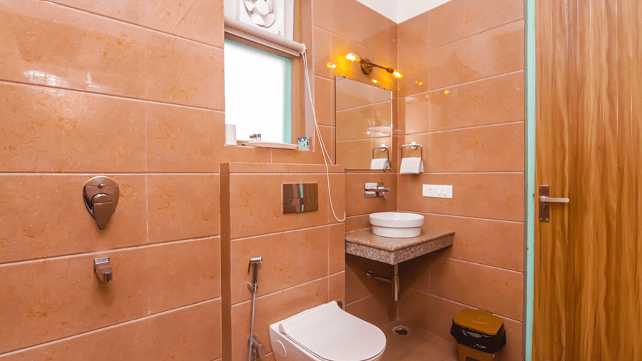 A compact bathroom at Vedikant Resorts The Mallard Corbett includes a sink, toilet, and shower area with wooden accents.