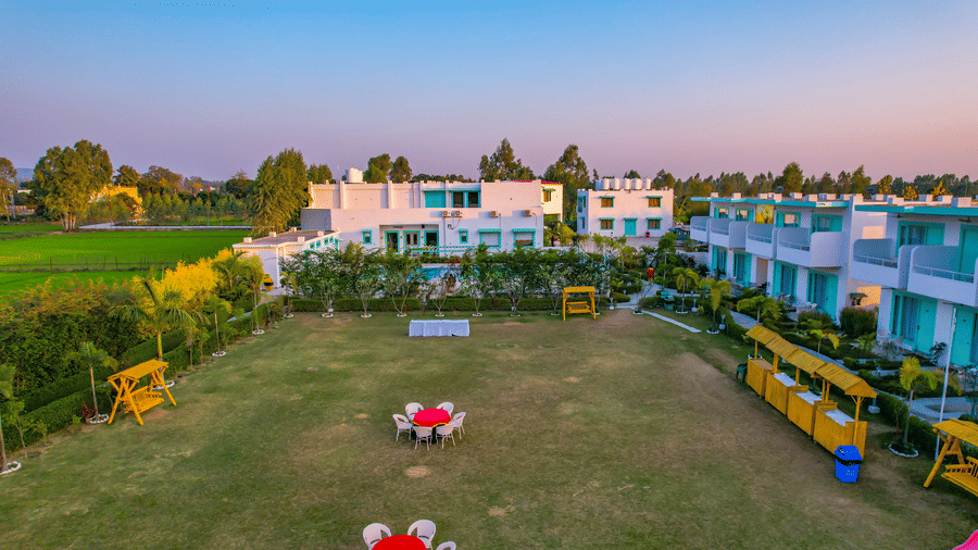 Lawn area at Vedikant Resorts The Mallard Corbett with tables and chairs set up outdoors, bordered by hedges and facing the rooms.