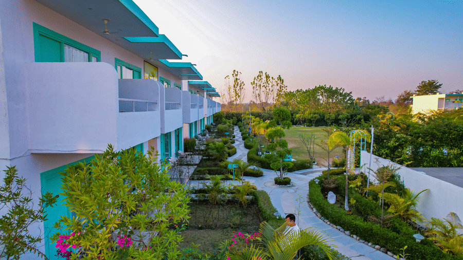 Walkway at Vedikant Resorts The Mallard Corbett with garden plants, white boundary walls, and rooms on the upper and lower floors.