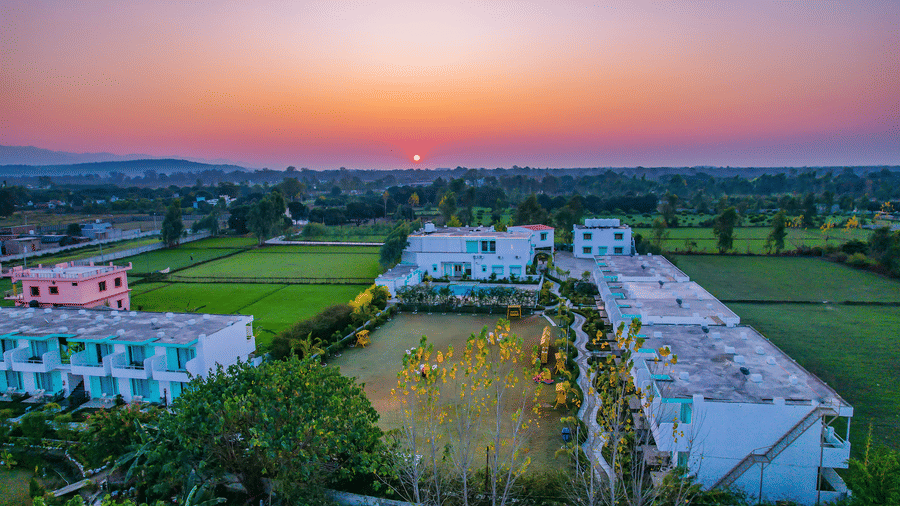 An aerial view of Vedikant Resorts The Mallard Corbett at sunset shows buildings and surrounding greenery.