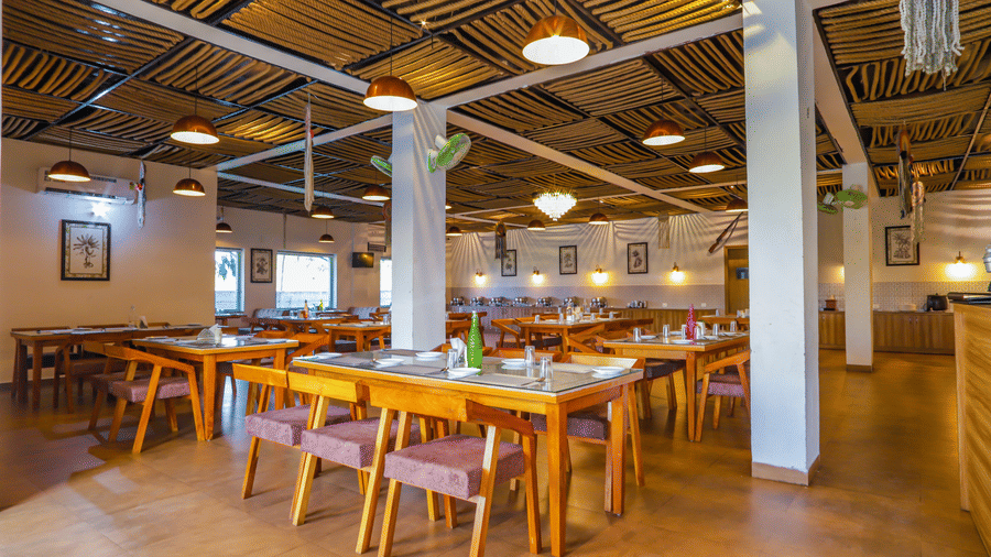 A bright dining hall at Vedikant Resorts The Mallard Corbett features wooden tables and colorful chairs.
