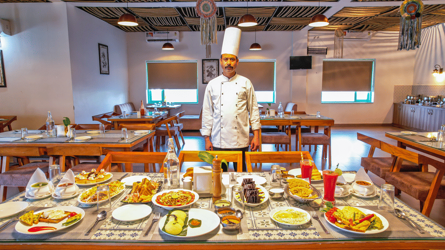 A chef stands near tables laden with food in a dining area at Vedikant Resorts The Mallard Corbett.