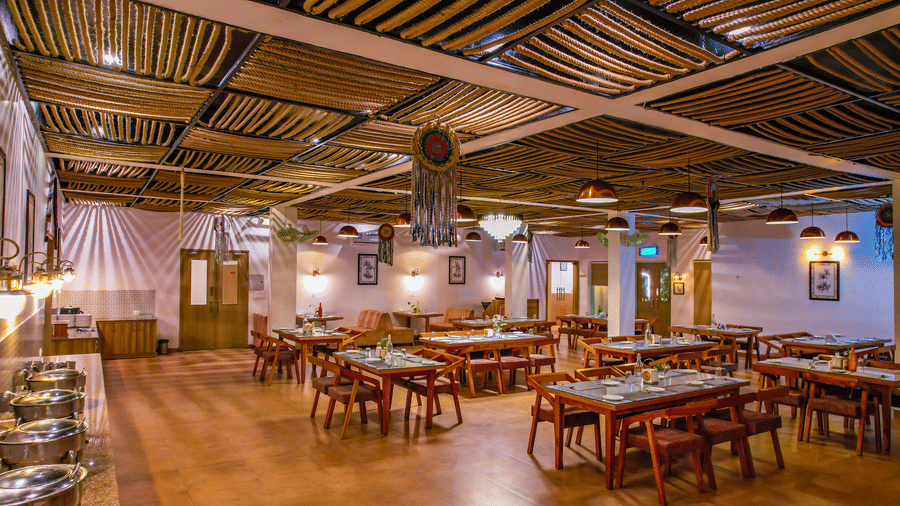 A spacious dining hall at Vedikant Resorts The Mallard Corbett shows multiple tables and chairs under a unique ceiling design.