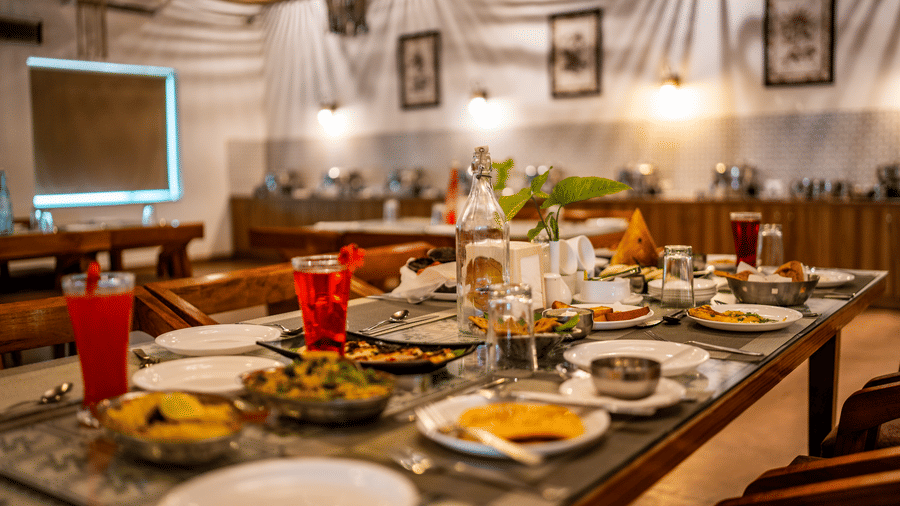 Himalayan Spices restaurant at Vedikant Resorts The Mallard Corbett featuring a dining table with different food items, chairs, surrounding it, and at a distance there is a food counter.