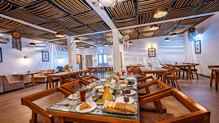 Himalayan Spices restaurant at Vedikant Resorts The Mallard Corbett featuring dining tables and chairs across the room. One of the dining tables have several dishes and beverages served.