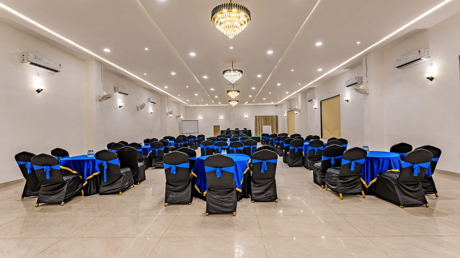 Mystic Jungle Hall at Vedikant Resorts The Mallard Corbett featuring each round tables surrounded by chairs, chandeliers, ceiling lights, fans, air-conditioner, and at the front there is a panel of table and chairs.