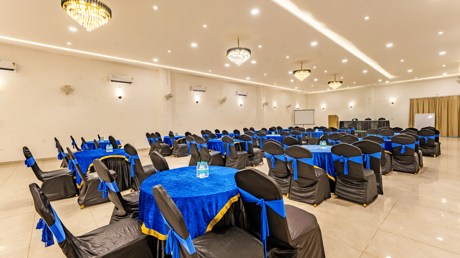 Mystic Jungle Hall at Vedikant Resorts The Mallard Corbett featuring each round tables surrounded by chairs, chandeliers, ceiling lights, fans, air-conditioner, and at the front there is a panel of table and chairs.