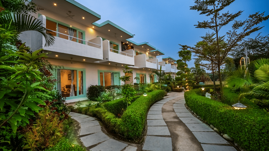 A pathway at Vedikant Resorts The Mallard Corbett featuring trees and plants on either side leading to the building of the property.