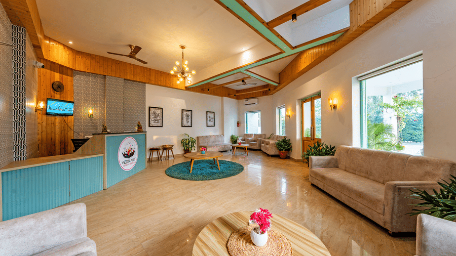Reception lobby at Vedikant Resorts The Mallard Corbett featuring a reception desk and a seating area featuring sofa sets, centre table with flower vase, and other decorative elements.