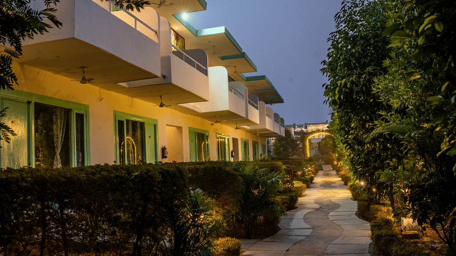 A pavement surrounded by trees of either side at Vedikant Resorts The Mallard Corbett featuring two storey buildings, each consisting of rooms.