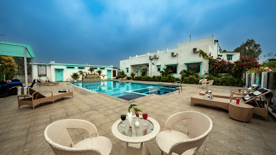 Seating area near the pool at Vedikant Resorts The Mallard Corbett featuring chairs and tables, lounger beds, and two storey building with room categories.