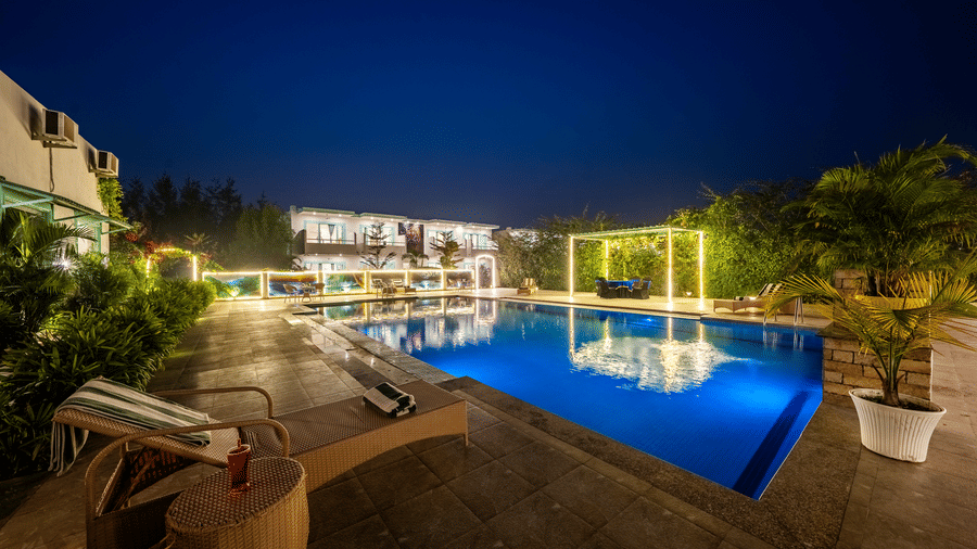 Swimming pool at Vedikant Resorts The Mallard Corbett featuring lounger beds, chairs, tables, and a well lit facade.