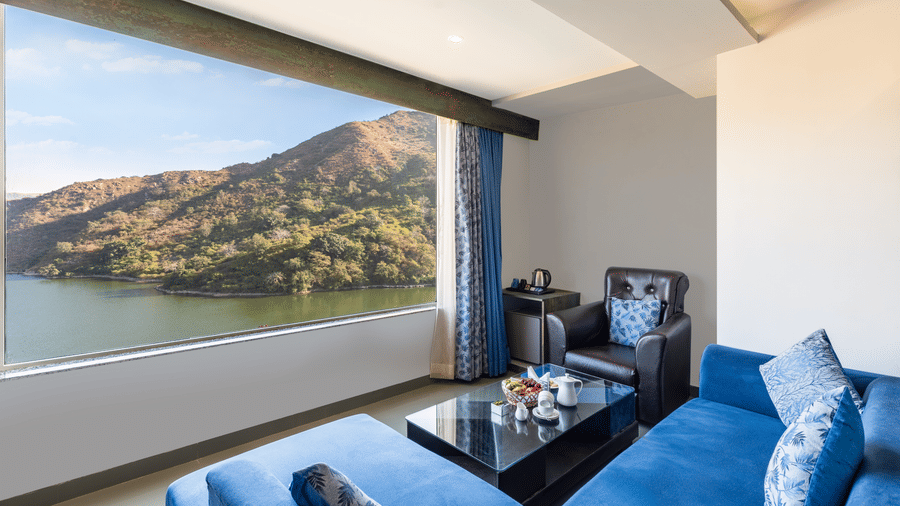 Living area with a blue couch and a large window with a view of mountain and water - Via Lakhela Resort & Spa