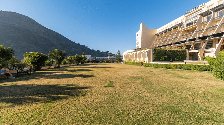 A wide shot of a building with a mountain backdrop in a green field - Via Lakhela Resort & Spa