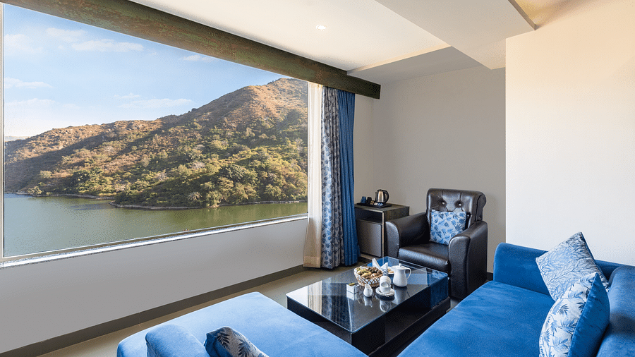 Living area with a blue couch and a large window with a view of mountain and water - Via Lakhela Resort & Spa