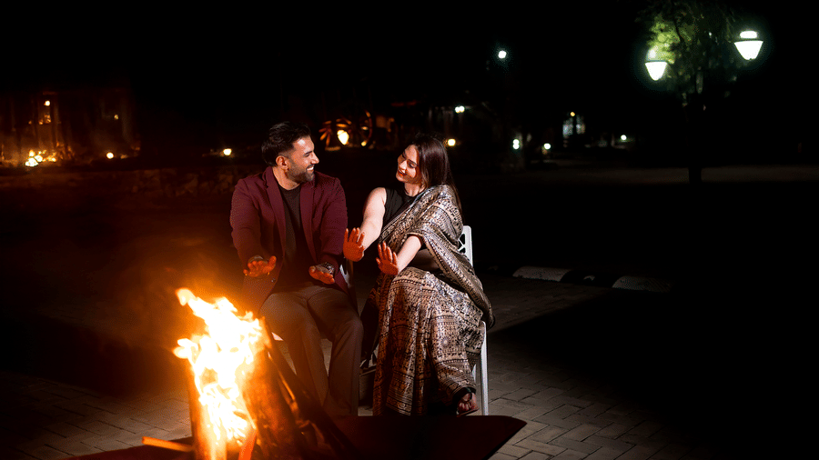 A man and a woman sitting near a brightly lit outdoor bonfire at night | Vintage Trails By Ilara