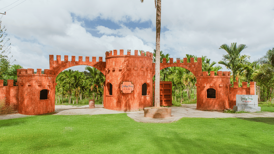 A decorative red brick castle-style wall structure built on a green lawn with palm trees in the background | Vintage Trails By Ilara