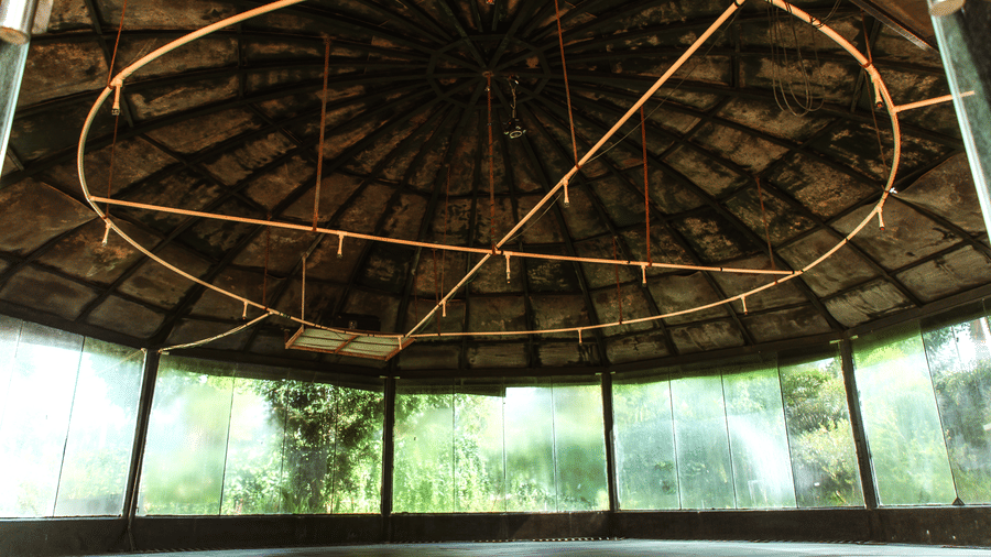 The interior view of a circular building featuring an exposed dome-style wooden ceiling structure and glass panels | Vintage Trails By Ilara