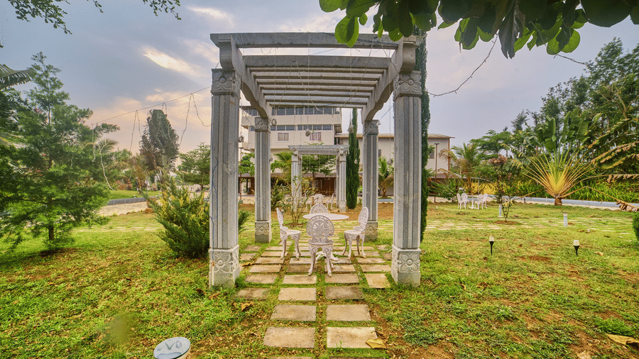 A pathway made of square stepping stones leading towards a modern, open-sided structure with a swing seat, set in a green garden - Vintage Trails By Ilara