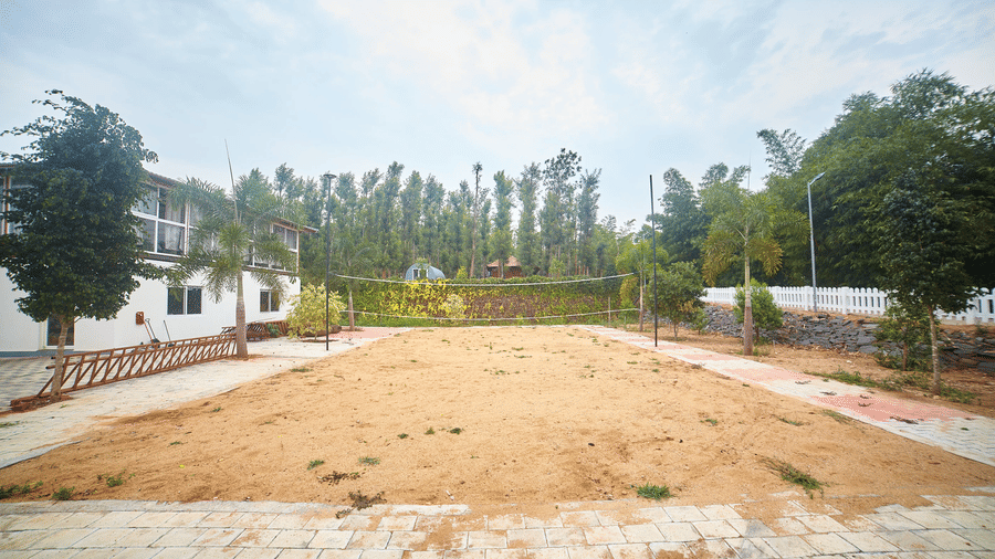 A wide, open expanse of dry, light brown ground, possibly a sports field or open space, with buildings and trees in the background under a pale sky - Vintage Trails By Ilara