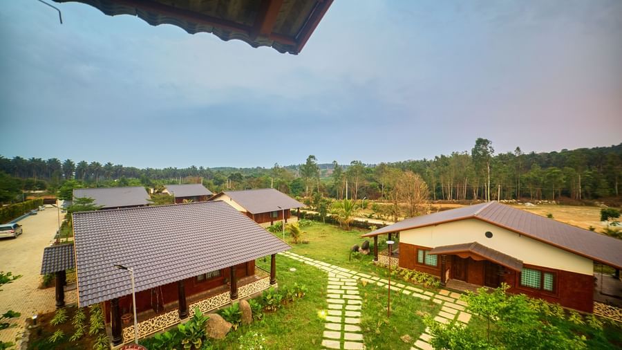 An aerial or elevated view of a resort with several traditional-style cottages with dark roofs, connected by grassy pathways, surrounded by green landscaping under a slightly overcast sky. - Vintage Trails by Ilara