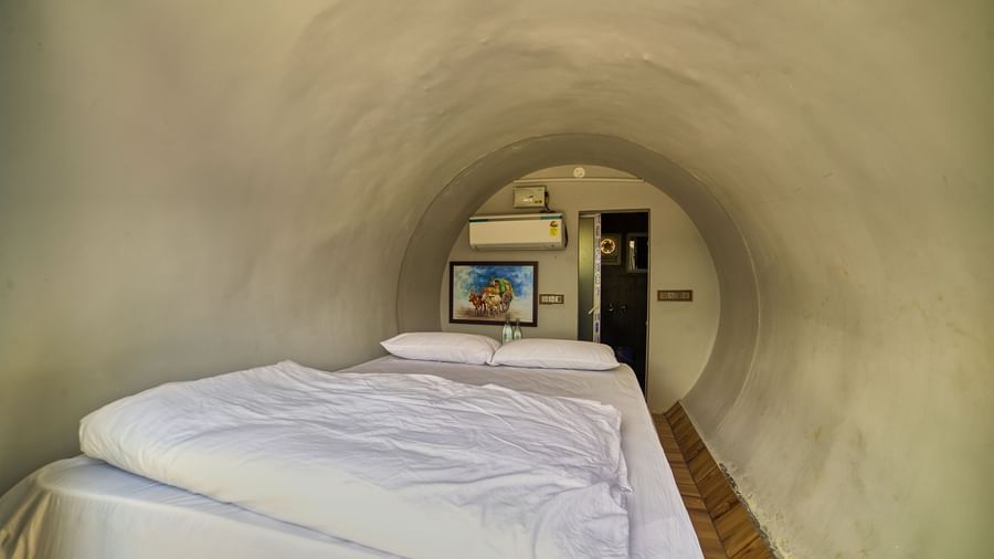The interior of a modern, capsule-style accommodation unit with a white bed positioned within a curved, light-coloured space, and a small mirror on the wall. - Vintage Trails by Ilara