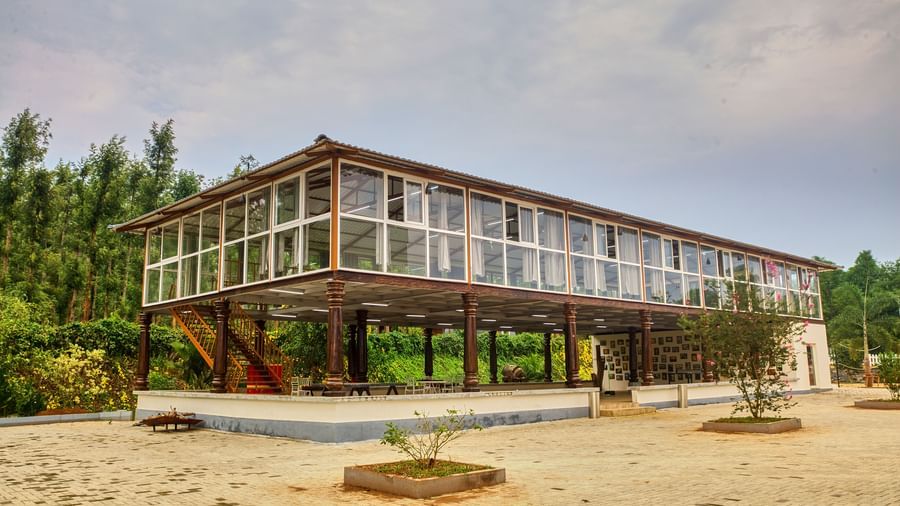 The exterior of a unique multi-level building with an open, modern design, set on a reddish-brown dirt area, with distant greenery and a cloudy sky. - Vintage Trails by Ilara