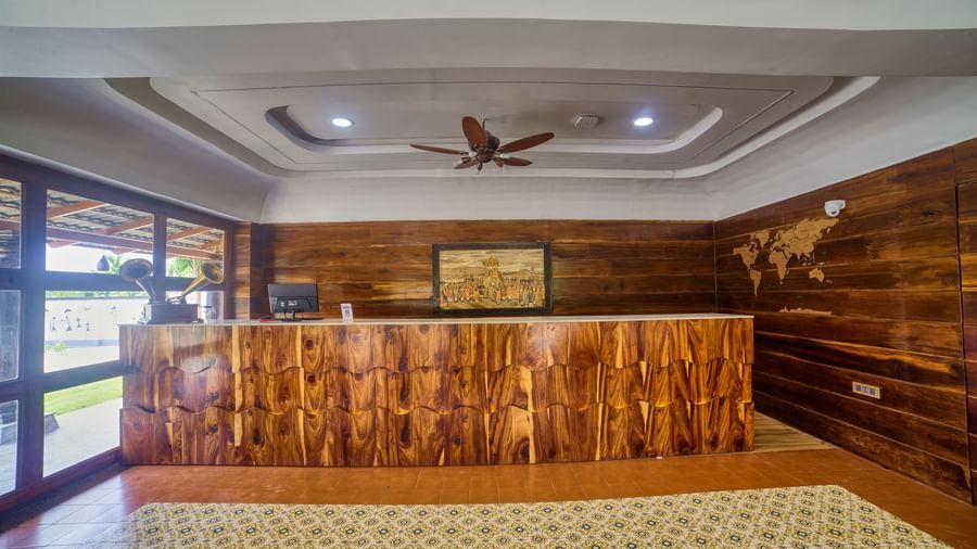 The reception desk of a hotel or resort, made of decorative wood, set against a wooden wall in a brightly lit room with a patterned floor. - Vintage Trails by Ilara