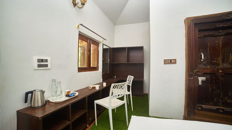 A bright hotel room featuring a bed with white linens, wooden furniture including a cabinet, and a white chair, viewed from a slightly different angle. - Vintage Trails by Ilara