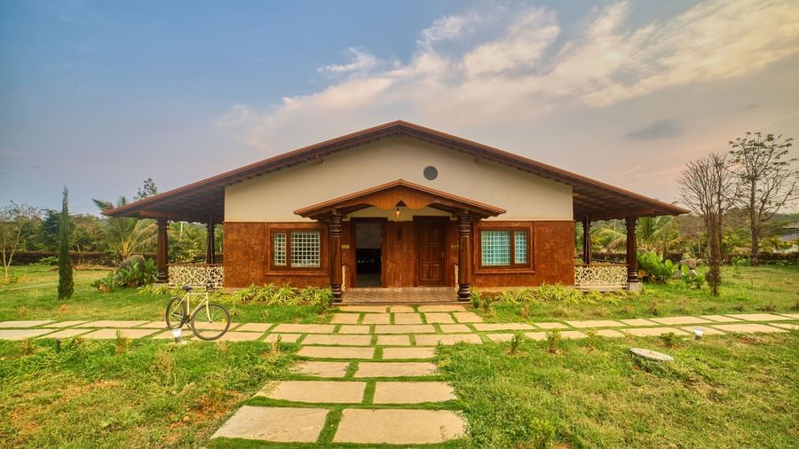 The front exterior of a single-storey building with a sloping roof and a prominent entrance, accessed by a path of large stepping stones through a green lawn. - Vintage Trails by Ilara