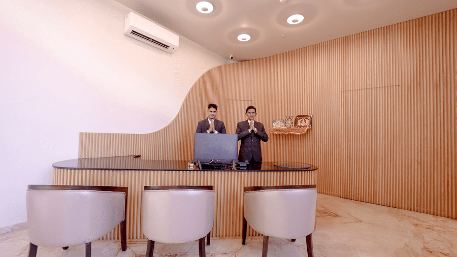 Guests are welcomed by 2 bowing staff behind the polished desk in the brightly lit, modern reception area of Vinti Resort, Ambaji.